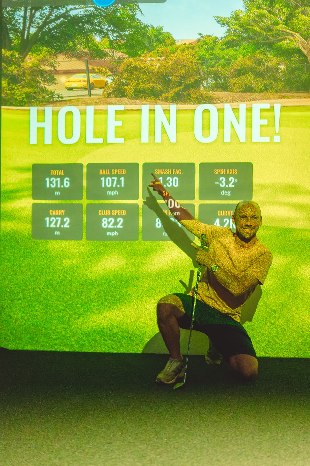 Guest kneeling in front of a simulator screen showing a hole in one