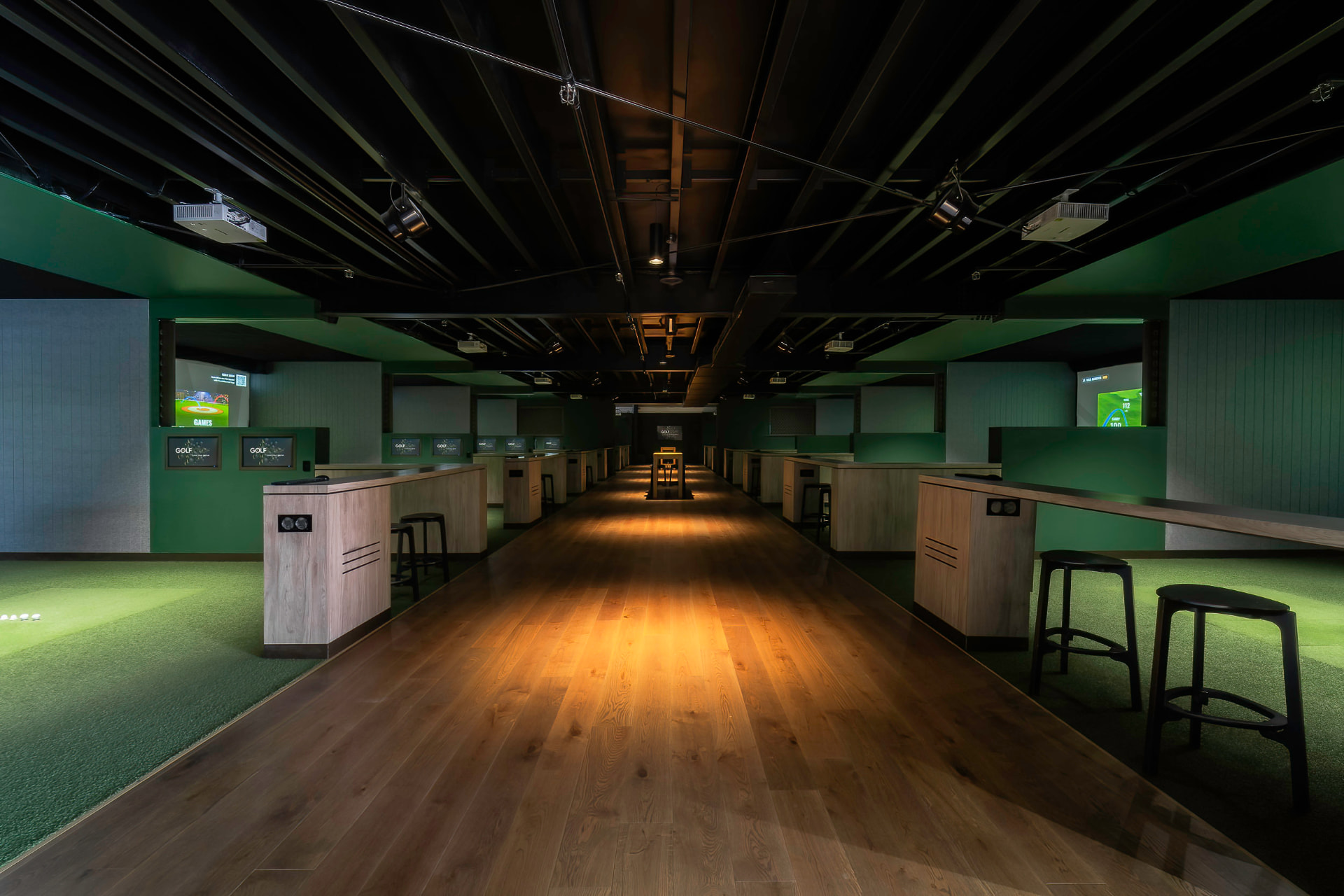 Wide view of the GolfSpace simulator floor with bays lining a wooden walkway